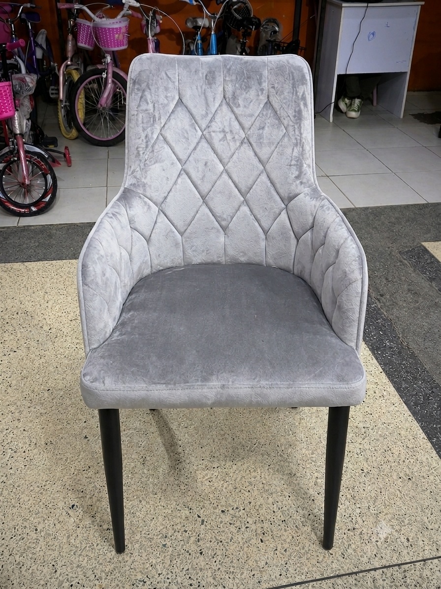 Modern grey velvet dining chair with diamond-tufted backrest, padded seat, armrests, and black wooden legs for dining rooms and restaurants.