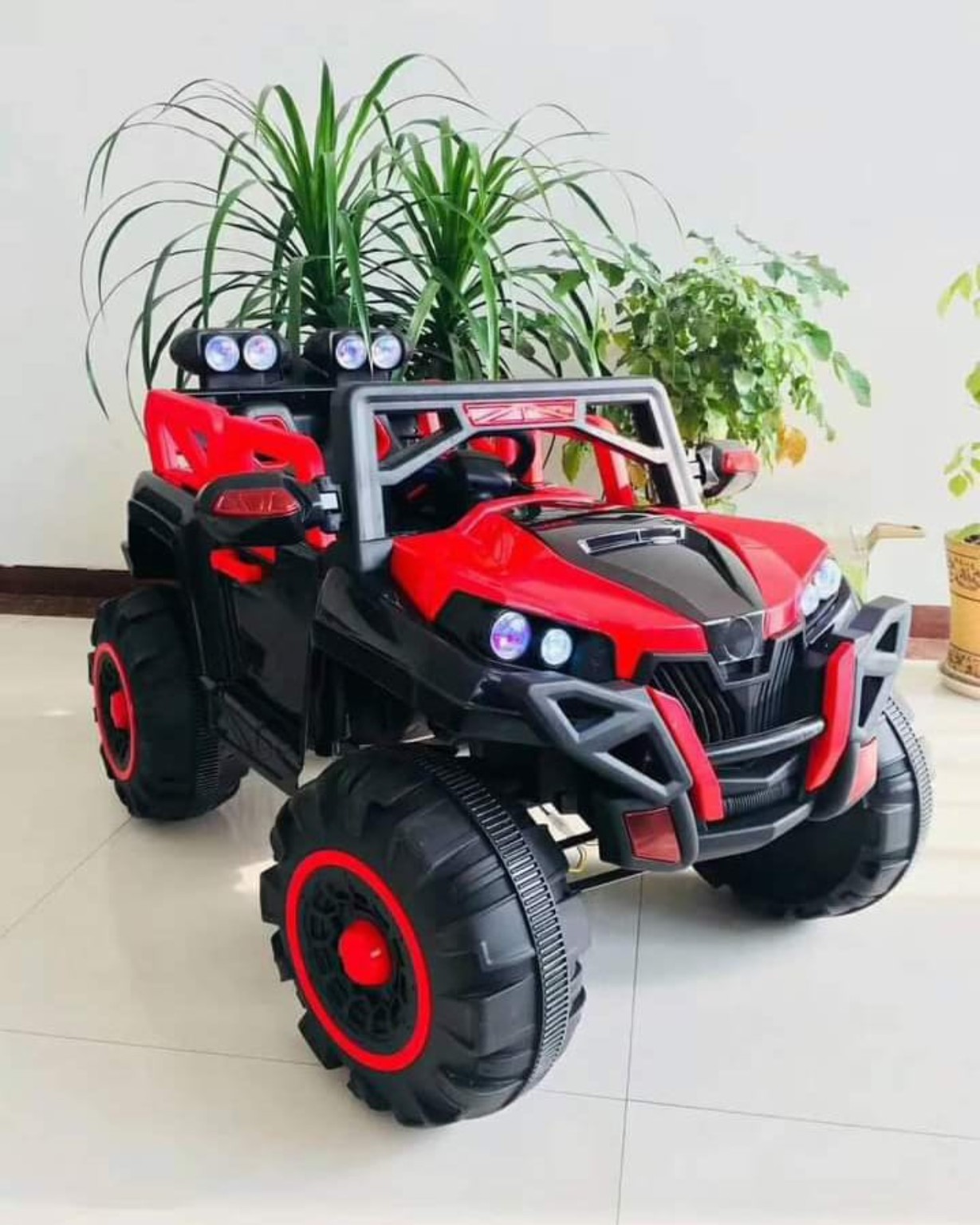 Red 2-seater kids electric ride-on off-road car with LED headlights, roof spotlights, oversized tyres, and realistic SUV styling.